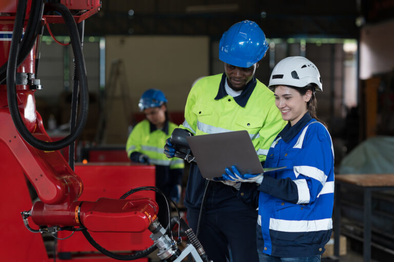 Male and female engineer workers control robot arm system welding with laptop computer at production plant factory